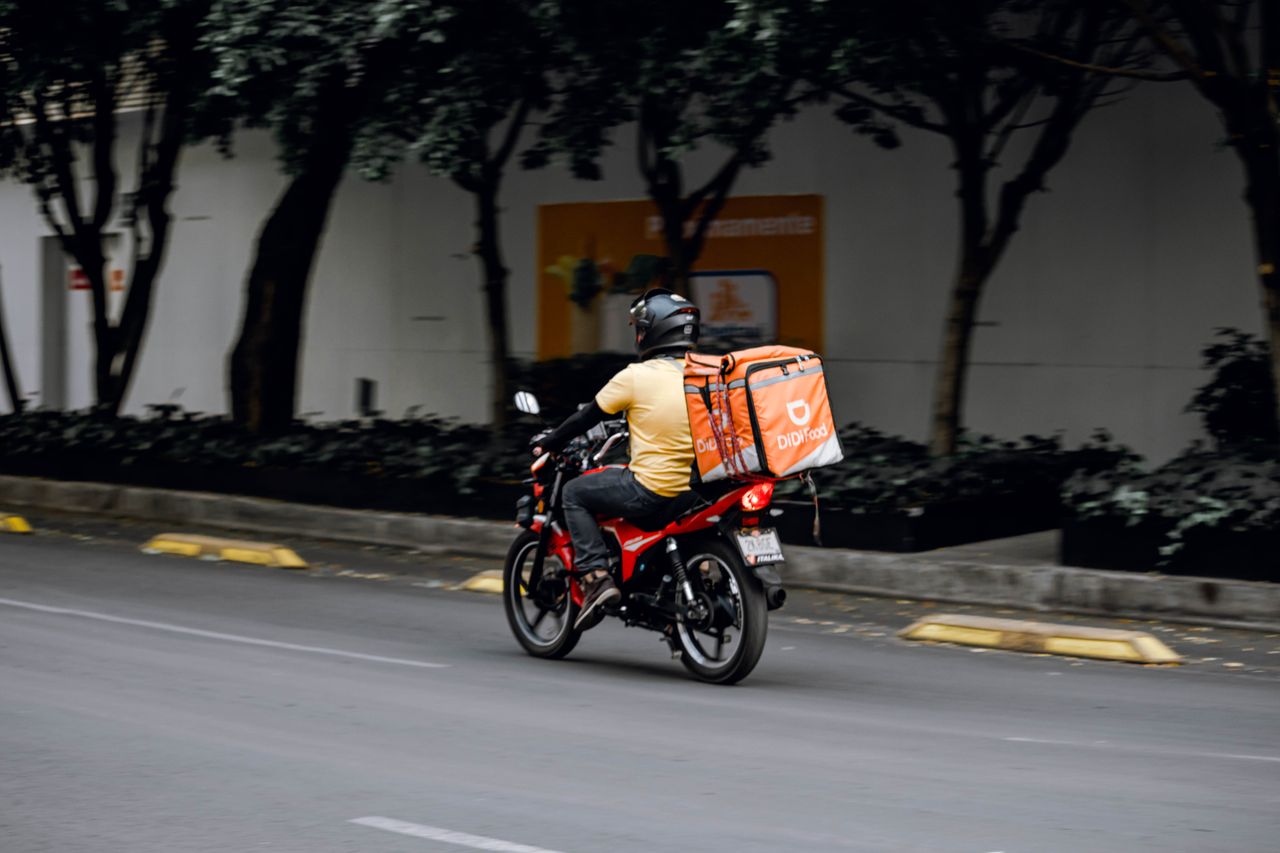 About A delivery man riding a motorcycle with a thermal bag on a city street during the day.
